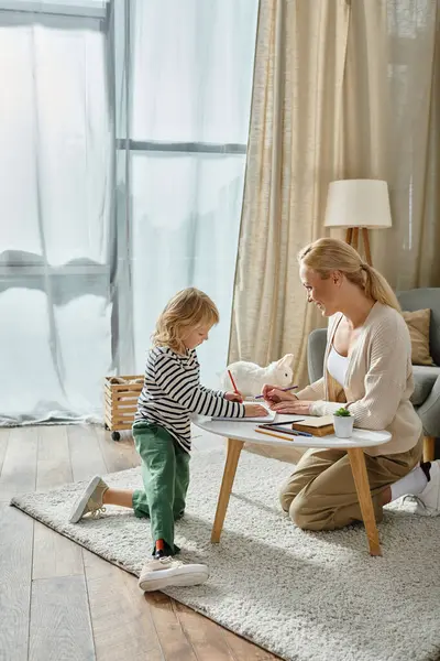 Glückliche Mutter schaut ihre Tochter mit Beinprothese auf Papier mit Buntstift an — Stockfoto