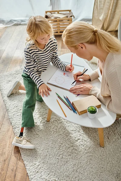 Madre e hijo con la pierna protésica dibujando juntos en papel con lápices de colores, tiempo de calidad - foto de stock