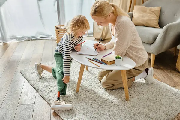 Madre e hija con el dibujo de la pierna protésica en papel con lápices de colores, tiempo de calidad - foto de stock