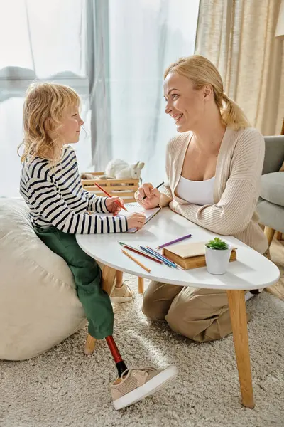 Mother and kid with prosthetic leg drawing on paper with colorful pencils together, quality time — Stock Photo