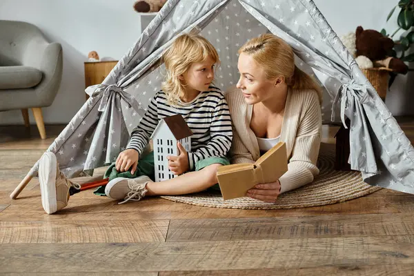 Kleines Mädchen mit Beinprothese und blonder Mutter liest Buch und sitzt zu Hause im Spielzelt — Stockfoto