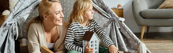Menina sonhadora e sua mãe alegre olhando embora ao ler o livro e sentado em jogar tenda, banner — Fotografia de Stock