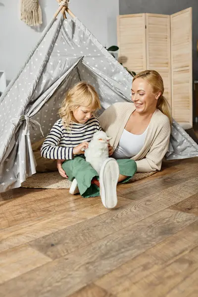 Blondes Mädchen mit Beinprothese spielt im Spielzelt mit Stoffkaninchen in der Nähe der Mutter — Stockfoto