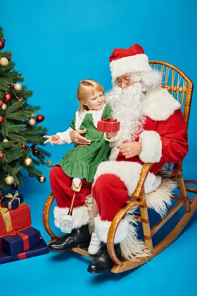 Glückliches Mädchen mit Beinprothese, das vom Weihnachtsmann neben dem geschmückten Weihnachtsbaum beschenkt wird — Stockfoto