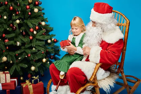 Happy girl with prosthetic leg sitting on laps of Santa Claus with present next to Christmas tree — Stock Photo