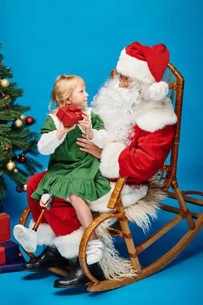 Chica alegre con la pierna protésica sentado en vueltas de Santa Claus con regalo al lado del árbol de Navidad - foto de stock