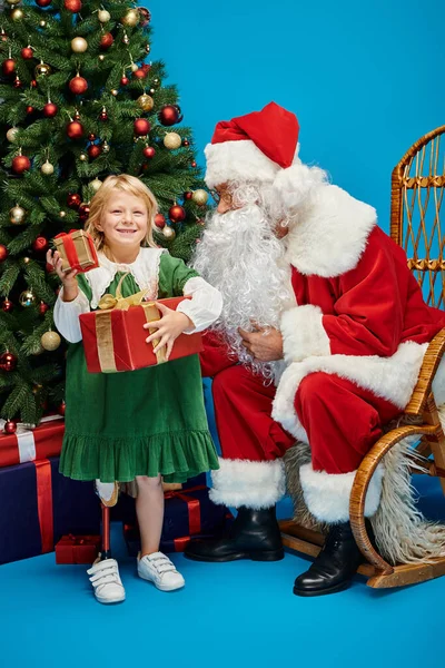 Санта Клаус дарит подарки счастливой девушке с протезной ногой рядом с рождественской ёлкой на голубом — стоковое фото