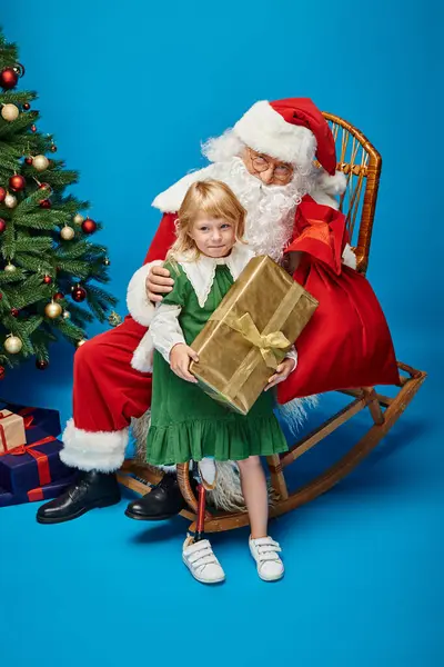 Санта Клаус дарит подарок счастливой девушке с протезной ногой рядом с рождественской ёлкой на голубом — стоковое фото