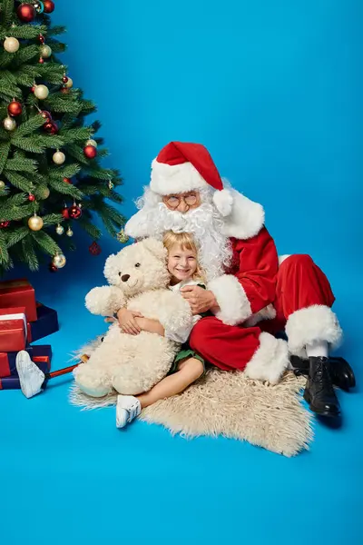 Happy girl with prosthetic leg and teddy bear sitting with Santa Claus next to Christmas tree — Stock Photo