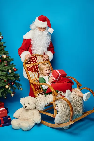 Weihnachtsmann Schaukelstuhl mit aufgeregtem Mädchen mit Beinprothese in der Nähe von Teddybär und Weihnachtsbaum — Stockfoto