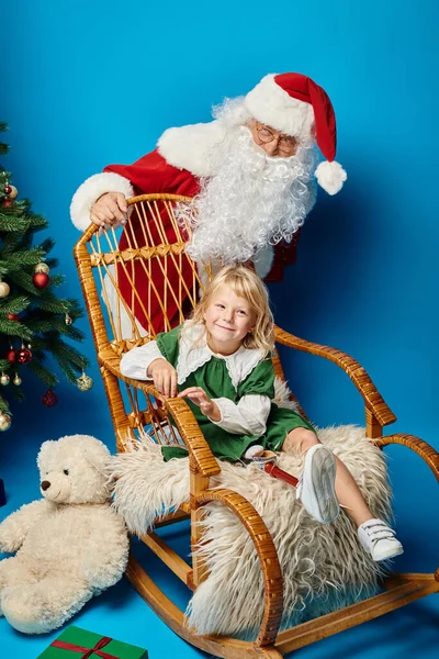 Chaise à bascule Père Noël avec fille heureuse avec jambe prothétique à côté de l'ours en peluche et arbre de Noël — Photo de stock