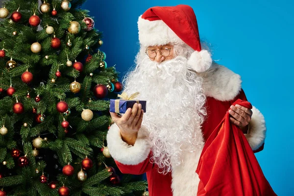 Santa Claus with beard and eyeglasses in red costume holding sack bag and Christmas present — Stock Photo
