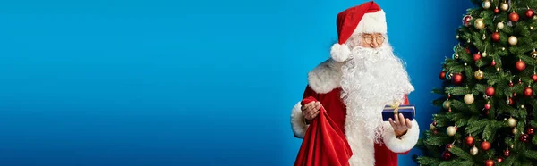 Santa Claus with beard and eyeglasses in red costume holding sack bag and Christmas present, banner — Stock Photo