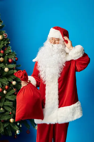 Happy Santa Claus with beard and eyeglasses in red costume holding sack bag with Christmas presents — Stock Photo