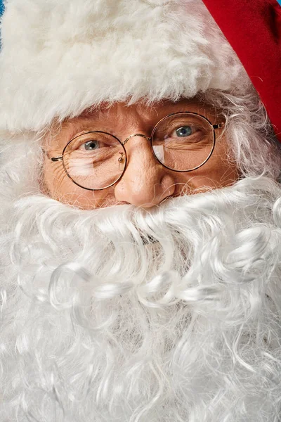Primer plano de Santa Claus feliz con barba blanca y anteojos mirando a la cámara sobre fondo azul - foto de stock