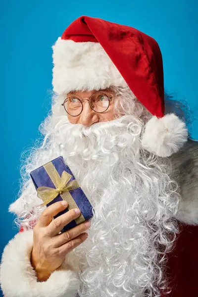 Retrato de Papai Noel feliz com barba branca e óculos segurando presente de Natal em azul — Fotografia de Stock