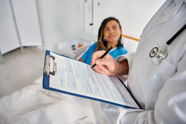 Attraente donna afro-americana sdraiata a letto nel reparto ospedaliero parlando con il suo giovane medico indiano — Foto stock