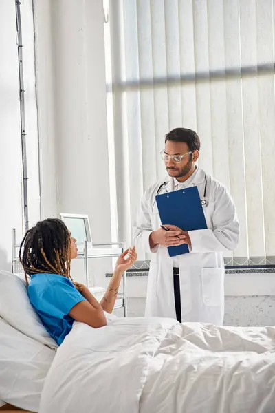 Handsome indian doctor in glasses talking to young african american patient in hospital, healthcare — Stock Photo