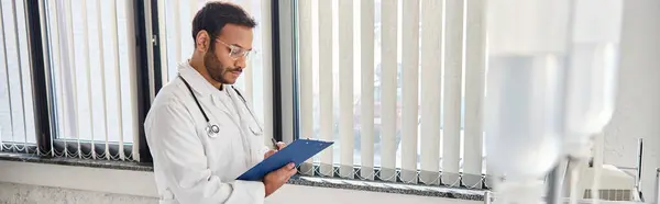 Giovane medico indiano con occhiali e stetoscopio nel reparto ospedaliero prendendo appunti, assistenza sanitaria, banner — Foto stock