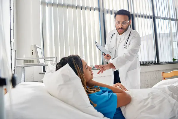 Intelligente medico indiano parlando con il suo afro-americano paziente femminile sdraiato a letto in reparto, assistenza sanitaria — Foto stock