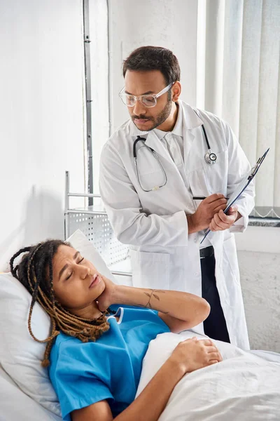 Молодой индийский врач смотрит на африканского американского пациента, лежащего в постели в больничном отделении, здравоохранения — стоковое фото