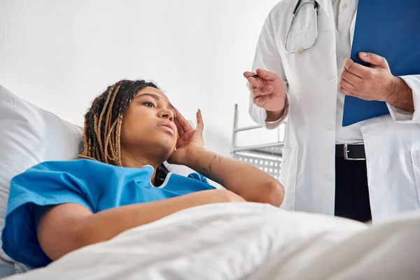 Sick african american woman lying in bed in hospital ward listening to her young indian doctor — Stock Photo