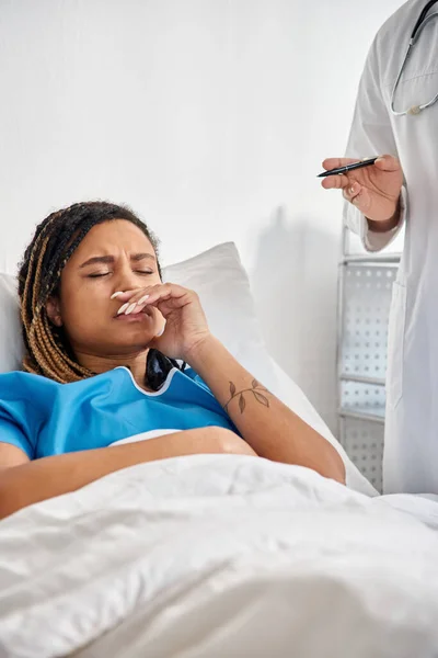 Malade afro-américaine femme couchée dans le lit à l'hôpital en écoutant son jeune médecin indien — Photo de stock