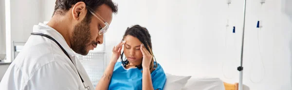 Concentrarsi sul giovane medico indiano seduto sul letto vicino al suo paziente afroamericano offuscato, striscione — Foto stock