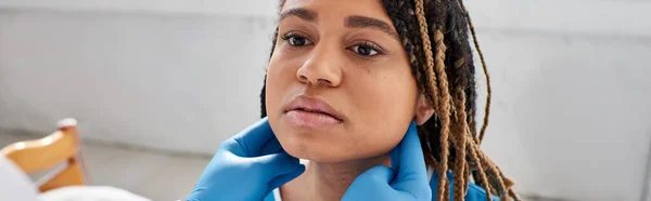 Giovane donna afroamericana guardando il suo medico indiano mentre esaminava i suoi linfonodi, striscione — Foto stock