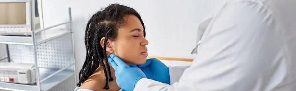 Young indian doctor examining lymph nodes of his ill african american female patient, banner — Stock Photo