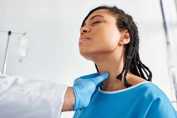 Sick pretty african american woman closing eyes while her indian doctor examining her lymph nodes — Stock Photo