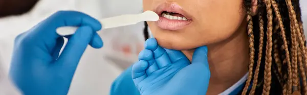 Vista ritagliata del medico che controlla la gola della sua giovane paziente afroamericana, banner — Foto stock