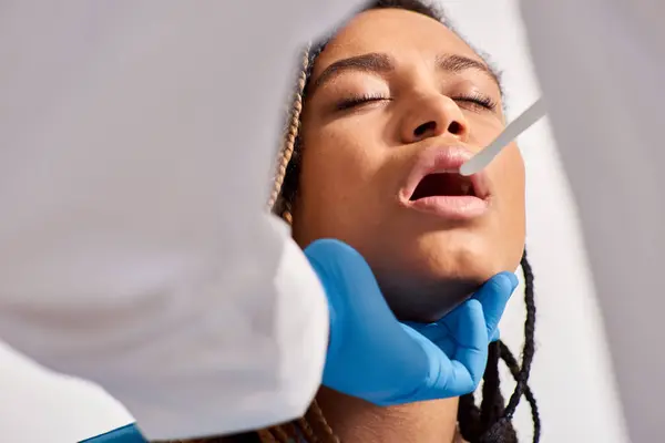 Vista ritagliata del medico che controlla la gola della sua giovane paziente afro-americana, assistenza sanitaria — Foto stock