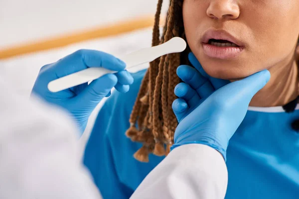 Vue recadrée de la jeune femme afro-américaine malade en salle d'hôpital ayant médecin contrôle de la gorge — Photo de stock