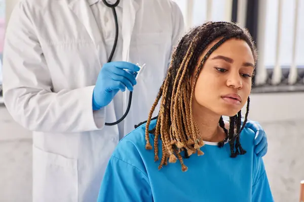 Médico indio escuchando el aliento de su paciente afroamericano enfermo con estetoscopio, atención médica - foto de stock