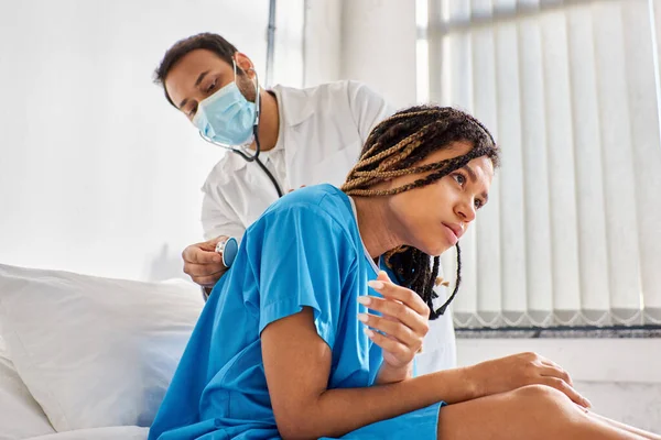 Giovane medico indiano che esamina alito di malato afro-americano paziente con stetoscopio, assistenza sanitaria — Foto stock