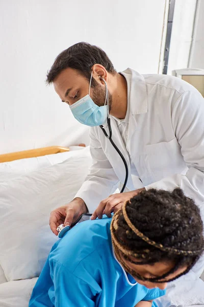 Young indian doctor examining breath of ill african american patient with stethoscope, healthcare — Stock Photo