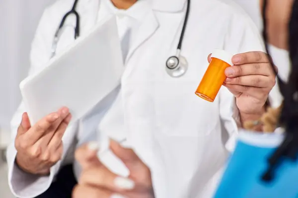 Vista recortada del médico indio sosteniendo tableta y pastillas frente a su paciente afroamericano - foto de stock