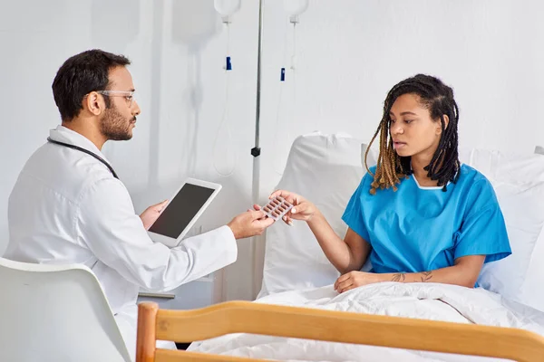 Indian doctor holding tablet and giving pills to his african american female patient, healthcare — Stock Photo