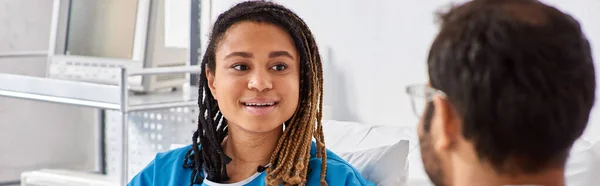 Concentrarsi sulla giovane donna afroamericana allegra guardando il suo medico indiano sfocato in reparto, striscione — Foto stock