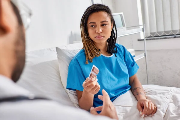 Fokus auf traurige afrikanisch-amerikanische Frau, die Pillen von ihrem verschwommenen indischen Arzt auf der Krankenhausstation nimmt — Stockfoto