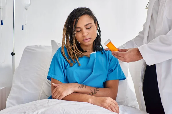 Cropped view of indian doctor giving pills to his depressed african american patient in bed — Stock Photo