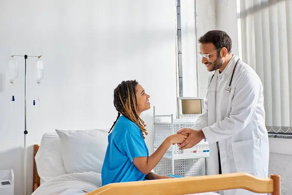 Jolly medico indiano in occhiali stringendo la mano con il suo allegro paziente afroamericano, assistenza sanitaria — Foto stock