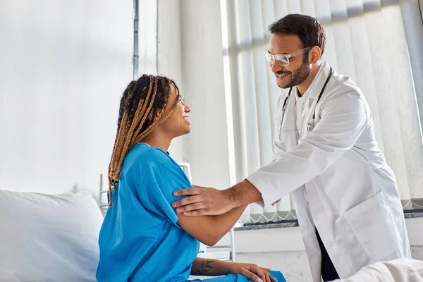 Jolly medico indiano in occhiali stringendo la mano con il suo allegro paziente afroamericano, assistenza sanitaria — Foto stock
