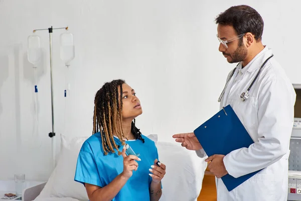 Молодой индийский врач обучает своего больного африканского пациента-американку, как использовать ингалятор от астмы — стоковое фото