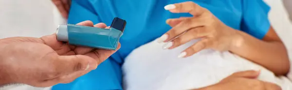 Vista recortada de la mujer afroamericana acostada en la cama mientras el médico enseña su uso inhalador, pancarta - foto de stock