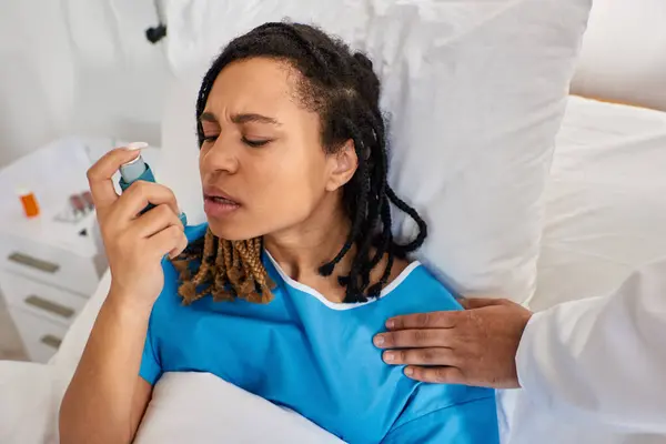 Young african american woman using her asthma inhaler with her indian doctor hand on shoulder — Stock Photo