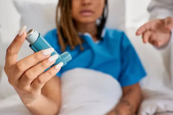Se centran en el inhalador de asma en manos de una paciente afroamericana con médico a su lado en la sala - foto de stock