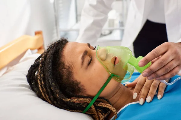 Vista recortada de médico reconfortante mujer afroamericana enferma acostada en la cama de hospital con máscara de oxígeno - foto de stock