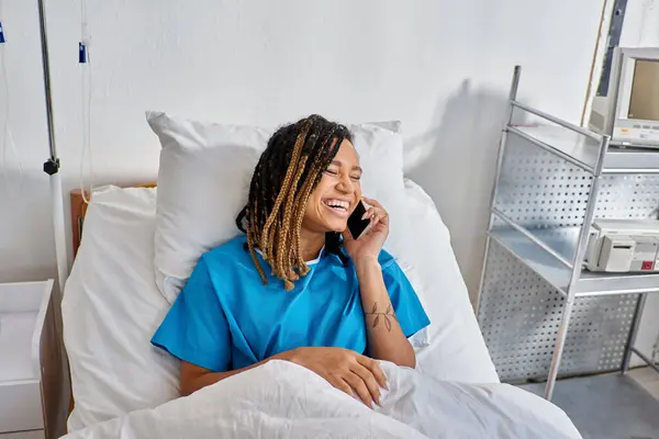Alegre jovem afro-americana falando por telefone e sorrindo em sua ala hospitalar, saúde — Fotografia de Stock